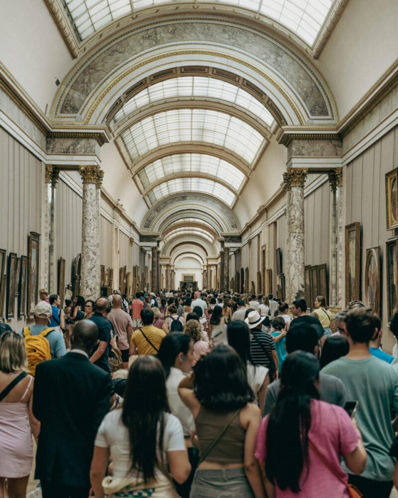 A bustling scene of tourists exploring the grand hallway of the Louvre Museum.