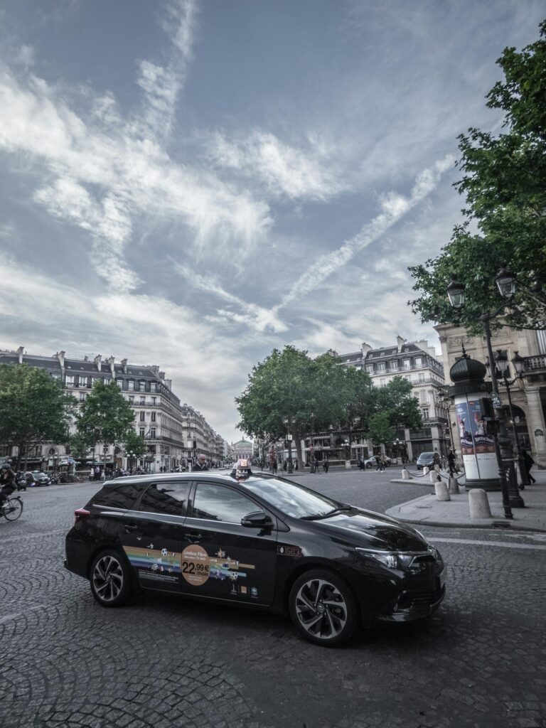 A sleek black car parked on a cobblestone street in Paris, capturing urban life and classic architecture.