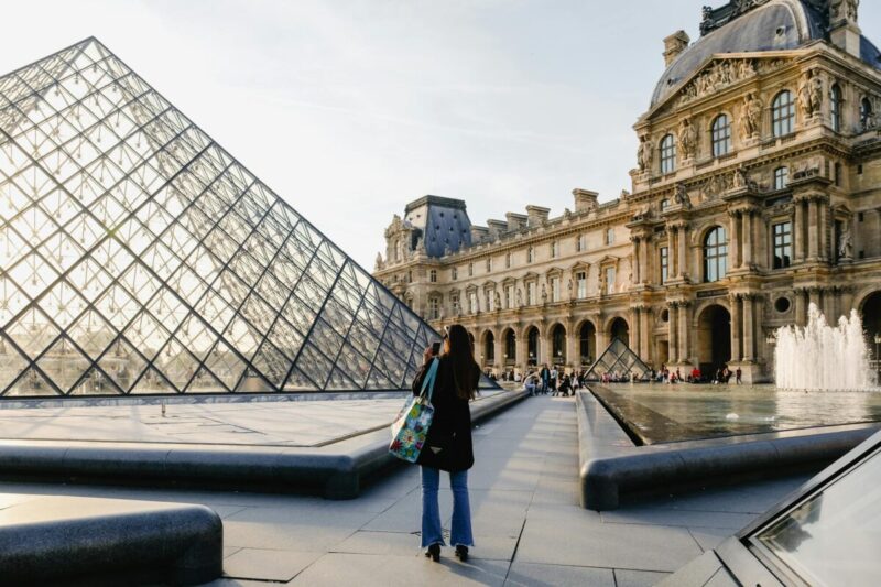 A tourist admires the iconic Louvre Pyramid and historic museum architecture, Paris.