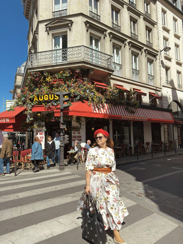 Stylish woman in floral dress walks by a Parisian café in bright daylight.