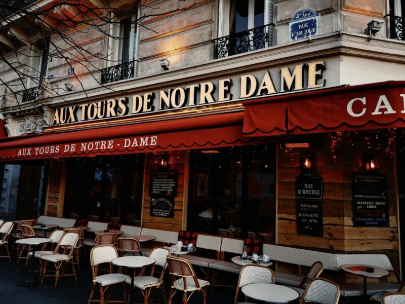 Parisian café exterior with warm lighting, showcasing outdoor seating and classic architecture.