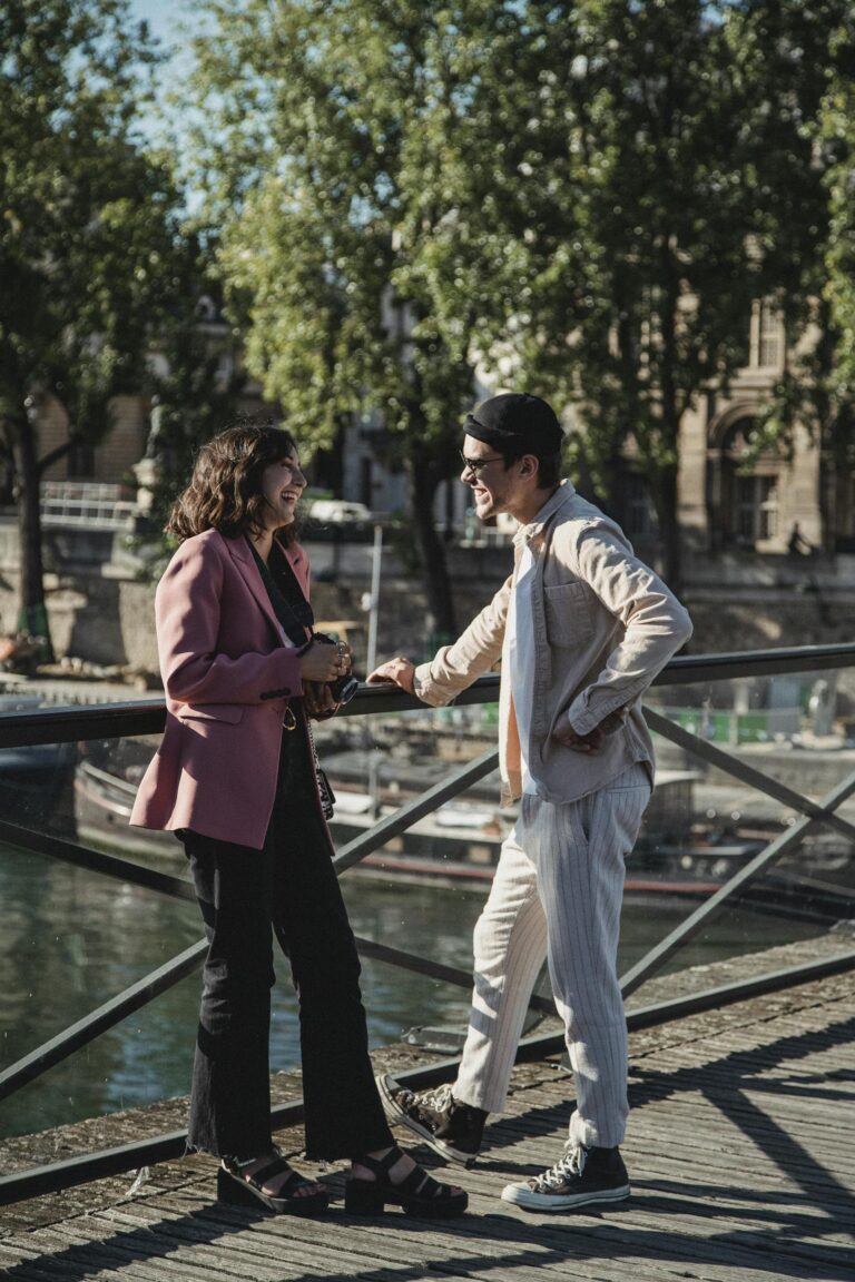 Happy couple shares a joyful moment by a riverside bridge in Paris under the sun.