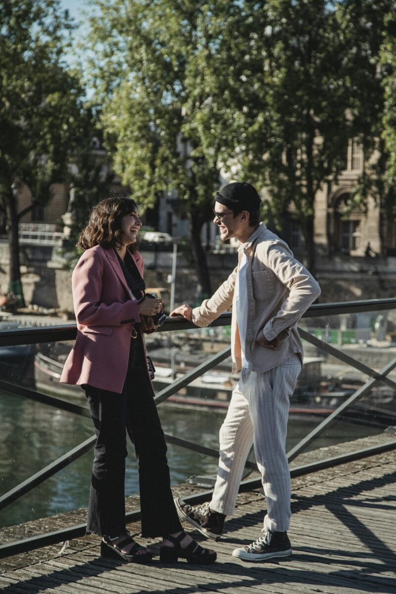 Happy couple shares a joyful moment by a riverside bridge in Paris under the sun.