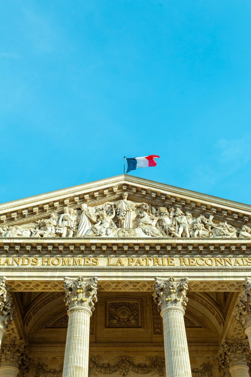 Detailed photograph of the Panthéon facade in Paris, France, showcasing its architecture under a clear blue sky.