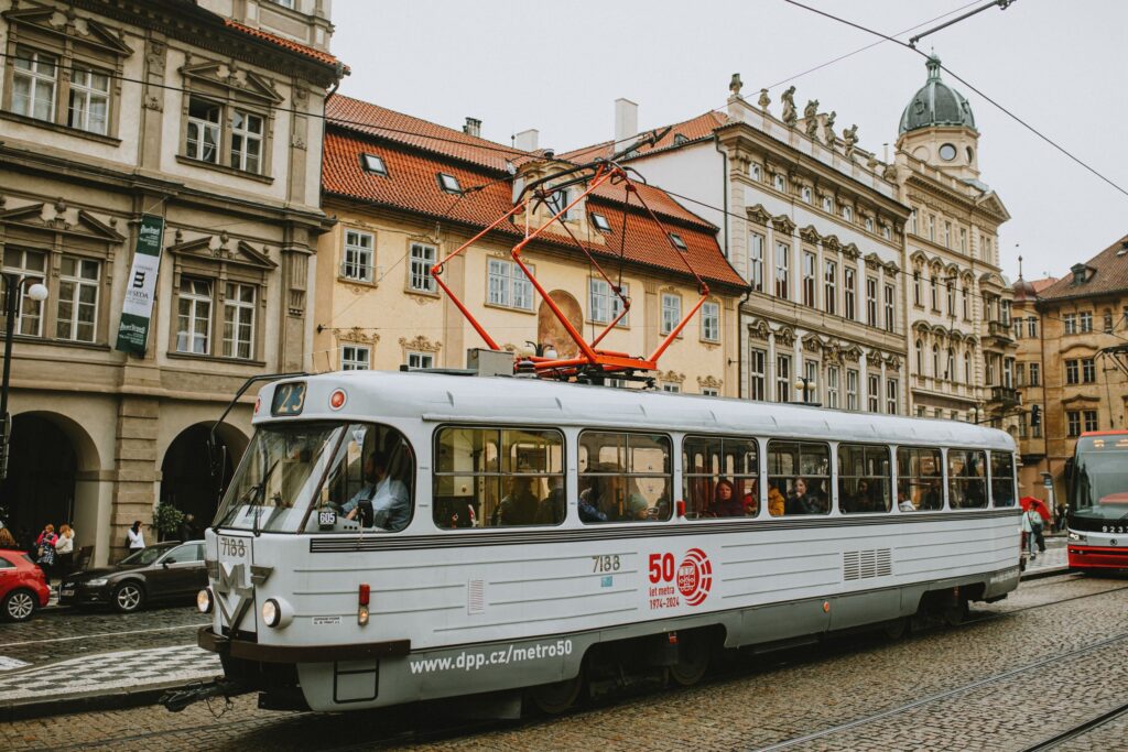 A vintage tram drives through a bustling street in Prague's historic district, surrounded by classic architecture.